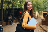 Fototapeta  - Pretty smiling casual student girl with books happily looking in camera in park