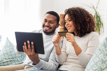 family, technology, online shopping and people concept - happy african american couple couple with tablet pc computer and credit card at home