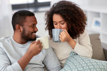 Leisure And People Concept - Happy African American Couple Drinking Coffee Or Tea At Home