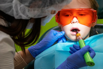 Little Caucasian girl treats teeth at the dentist in orange glasses