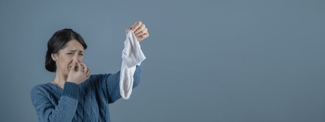 girl holds a bad smelling sock in her hand; foot odor