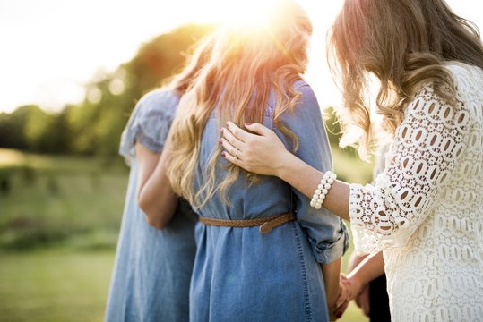 Closeup shot of females with their arms on each other while praying with a blurred background