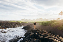 A Girl Walking On Lava Rocks Near The Ocean, Big Island, Hawaii