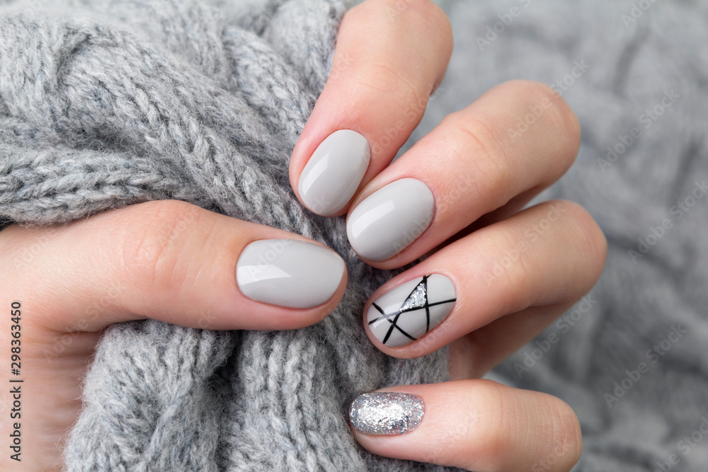 Fotografering Females hand with modern manicure holds gray knitted sweater  close up