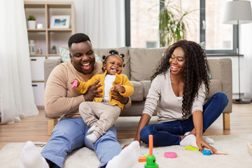 family, parenthood and people concept - happy african american mother, father and baby daughter playing with toy blocks at home