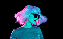 Nightlife, Fashion And People Concept - Happy Young Woman Wearing Pink Wig And Black Sunglasses In Neon Ultra Violet Light Dancing Over Black Background