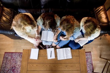 Overhead shot of females sitting while holding hands and reading the bible