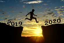 Silhouette Of Young Man Jump Between 2019 And 2020 Years, Over The Sunset And Through Gap Of Hill. Happy New Year Concept.