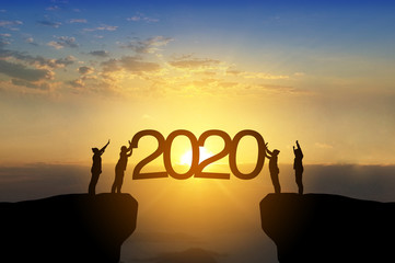 Silhouette image of happy teamwork standing on opposite sides of cliff use their hand push 2020 text to the sky like as set up year 2020 target.