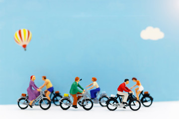 Miniature people enjoy riding a bicycle on blue background.