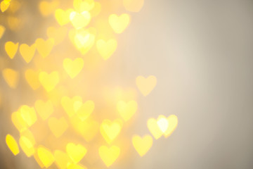 Blurred view of gold heart shaped lights on light background