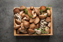 Different Wild Mushrooms In Wooden Crate On Grey Background, Top View