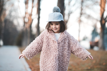 Wall Mural - Funny kid girl 3-4 year old wearing trendy winter coat in park. Walking child outdoors. Autumn season. Childhood.