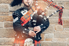 EDINBURGH, SCOTLAND, 24 March 2018 , Scottish Bagpiper Dressed In Traditional Red And Black Tartan Dress Stand Before Stone Wall. Edinburgh, The Most Popular Tourist City Destination In Scotland..