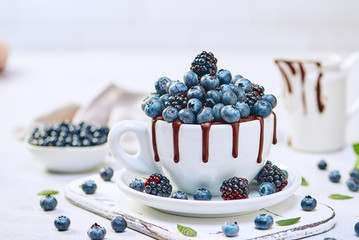 Chocolate mug cake with blueberries and blackberries in a white ceramic mug on white background