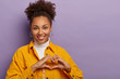 © wayhome.studio  - Kind lovely Afro American woman makes heart gesture, confesses in love, expresses sympathy and joy, has truthful feelings, wears stylish clothing, isolated over purple background. My heart is to you