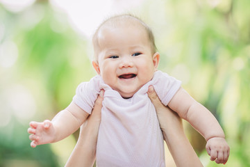 Wall Mural - Smiley face of newborn baby feeling happy and smiles with her mother in the garden. Portrait of Asian family.