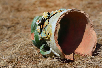 An old broken colored jug of clay lies on dry soil on the ground in Sicily