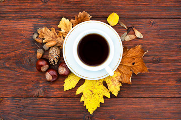 Cup of tea on a wooden table with autumn leaves, chestnuts and pine cones.