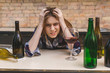 © denis_vermenko - Young sad and wasted alcoholic woman sitting at kitchen couch drinking red wine, completely drunk looking depressed lonely and suffering hangover in alcoholism and alcohol abuse.