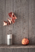 Autumn Background With Orange Decorative Pumpkins And Dry Sycamore Twig In Vase On Aged Wood Shelf On Rustic Wooden Wall