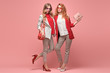 Two fashionable woman sisters in Trendy autumn red elegant outfit, stylish hair, makeup hugging. Gorgeous friends in jacket, heels on pink. Sensual model girl, stylish pastel fashion accessories