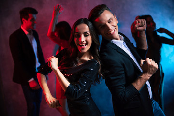 Sparkling mood. Young attractive girl in a black glittery dress is dancing back to back with a good-looking man, who is smiling broadly while looking at her.