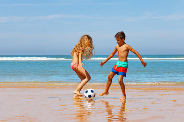 Two kids play soccer football ball on sand beach