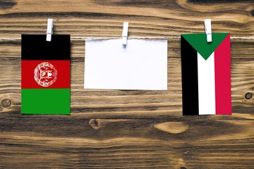 Wall Mural - Hanging flags of Afghanistan and Sudan attached to rope with clothes pins with copy space on white note paper on wooden background.Diplomatic relations between countries. Cooperation concept.