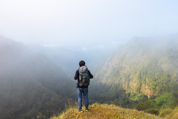 A backpack man standing on cliff and see over view in nature.Tourist  enjoying fresh air. A man enjoying free happiness in beautiful Thailand landscape.