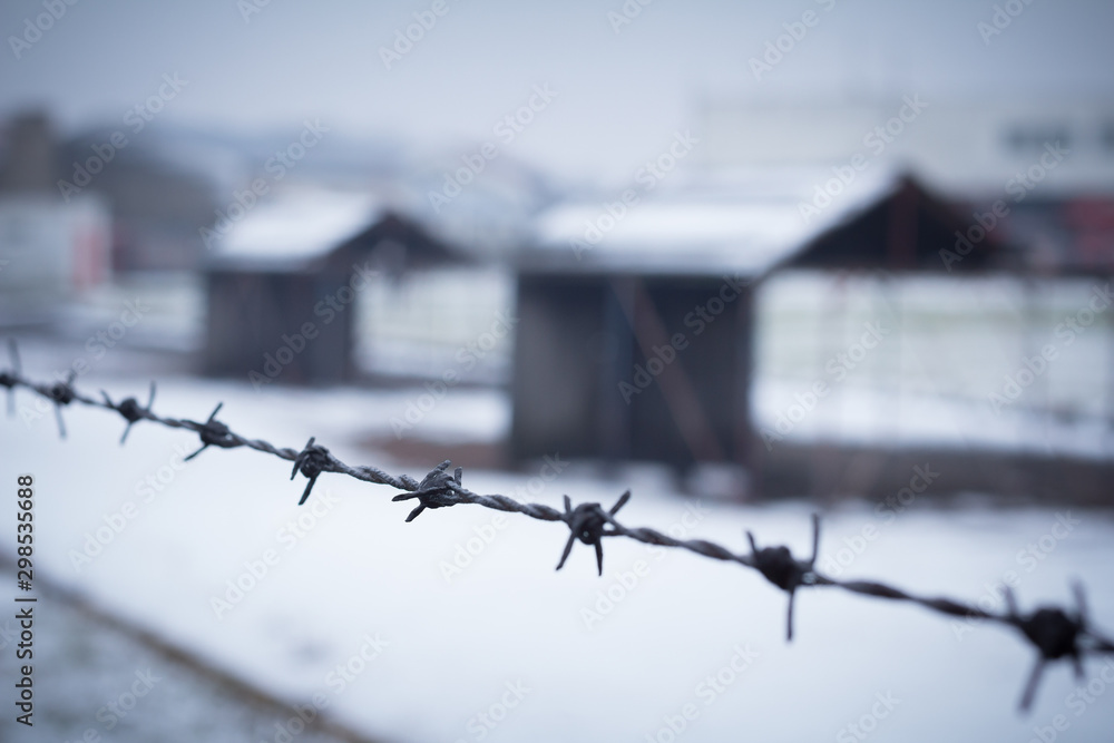 barbed wire closeup with detention camp in background - obrazy, fototapety, plakaty 