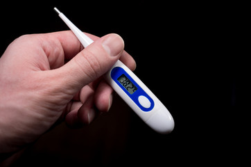 electronic thermometer in hand shows high temperature on the dark background, fever, disease