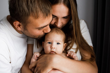 Young beautiful happy parents holding cute little baby and kissing her head