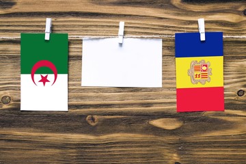 Hanging flags of Algeria and Andorra attached to rope with clothes pins with copy space on white note paper on wooden background.Diplomatic relations between countries.