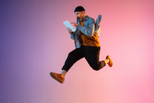 Full Length Portrait Of Happy Jumping Man Wearing Casual Clothes In Neon Light Isolated On Gradient Background. Emotions, Ad Concept. Using Tablet, Hurrying Up, Late For Work Or Sale, Shopping.