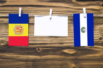 Hanging flags of Andorra and El Salvador attached to rope with clothes pins with copy space on white note paper on wooden background.Diplomatic relations between countries.