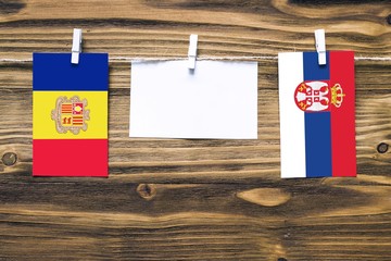 Hanging flags of Andorra and Serbia attached to rope with clothes pins with copy space on white note paper on wooden background.Diplomatic relations between countries.
