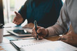 © wutzkoh - Business partnership coworkers writing cost work progress and using a tablet to analysis graph company financial budget report and planning for future in office room.
