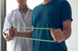 © wutzkoh - Patient doing stretching exercise with a flexible exercise band and a physical therapist hand to help in clinic room.