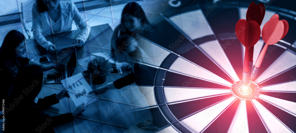 Business Target Goal For Success Strategy Concept - Red dart arrow hitting center goal on the dart board with business people working in background showing precision and success of business target. - obrazy, fototapety, plakaty 
