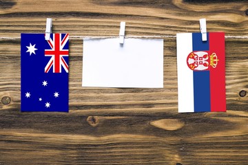 Wall Mural - Hanging flags of Australia and Serbia attached to rope with clothes pins with copy space on white note paper on wooden background.Diplomatic relations between countries.