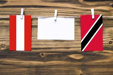 Wall Mural - Hanging flags of Austria and Trinidad And Tobago attached to rope with clothes pins with copy space on white note paper on wooden background.Diplomatic relations between countries.