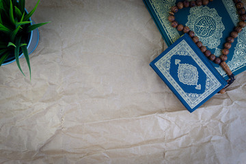 Poster - Flat lay Holy Quran with arabic calligraphy meaning of Al Quran and tasbih or rosary beads over wooden paper background. Selective focus and crop fragment