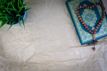 Poster - Flat lay Holy Quran with arabic calligraphy meaning of Al Quran and tasbih or rosary beads over wooden paper background. Selective focus and crop fragment