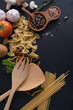 Flat lay Ingredients for cooking Italian pasta on black stone slate - fettuccine, spaghetti, tomatoes, basil, oil and garlic. Italian food. Top view with space for text.