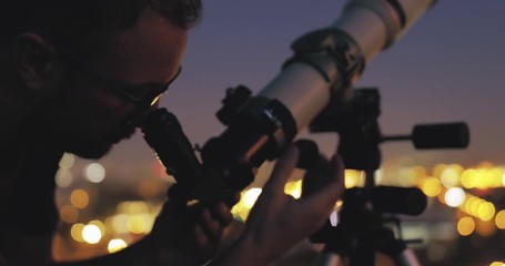 Wall Mural - astronomer with a telescope watching at the stars and moon with blurred city lights in the backgroun
