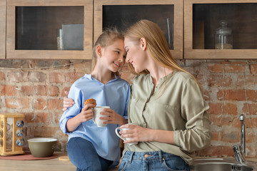 Happy mother and daughter sharing secrets while drinking tea