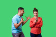 © khosrork - Furious man in casual wear standing with raised arms and desperately screaming near happy woman using phone and ignoring him, attracting her attention. isolated on green background, indoor studio shot