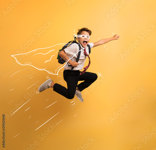 Fotografía Young boy student jumps high like a super hero. Yellow background