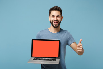 Young laughing man in casual clothes posing isolated on blue wall background in studio. People lifestyle concept. Mock up copy space. Hold laptop pc computer with blank empty screen, showing thumb up.